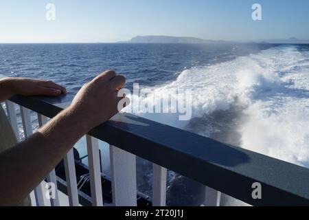 Balustrades de navire avec deux mains appuyées dessus. Sur le fond, il y a de l'eau de quille. Banque D'Images