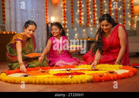 Joyeuse famille indienne multigénérationnelle préparant diwali rangoli sur le sol pour la célébration du festival diwali à la maison - concept de décoration traditionnelle Banque D'Images