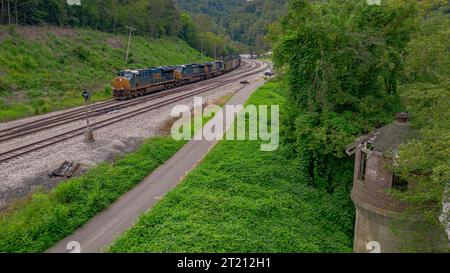 Un train de marchandises est capturé en mouvement sur un ensemble de voies ferrées qui mènent à une vieille tour abandonnée en arrière-plan Banque D'Images