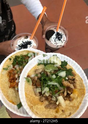 Deux tacos avec une variété de garnitures fraîches servies sur des assiettes blanches, avec deux boissons glacées dans des verres sur le côté Banque D'Images