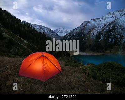 Une tente rouge, illuminée de l'intérieur, est installée dans un bel endroit haut dans les montagnes. Nuit dans la nature dans les montagnes Banque D'Images