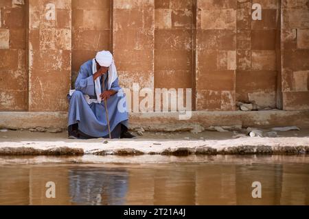 Un homme arabe d'âge moyen en robe traditionnelle sur un rebord de pierre surplombant l'eau Banque D'Images