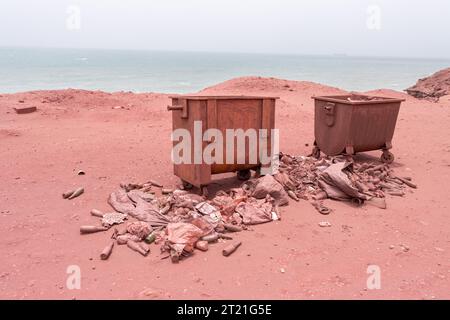 Plage rouge sur l'île d'Hormuz. Les ordures éparpillées autour de la poubelle sur la plage Banque D'Images