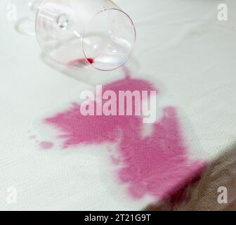 Verre de vin renversé avec une tache rouge sur la nappe Banque D'Images