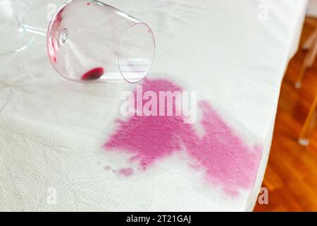 Verre de vin renversé avec une tache rouge sur la nappe Banque D'Images