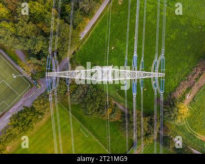 Pylône haute tension avec lignes électriques entre la nature et le terrain de sport photographié directement d'en haut avec drone Banque D'Images