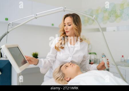 Portrait de femme esthéticienne docteur touchant l'écran tactile avec les doigts ajustant l'appareil de levage rf. Femme esthéticienne paramètres microneedle RF Banque D'Images