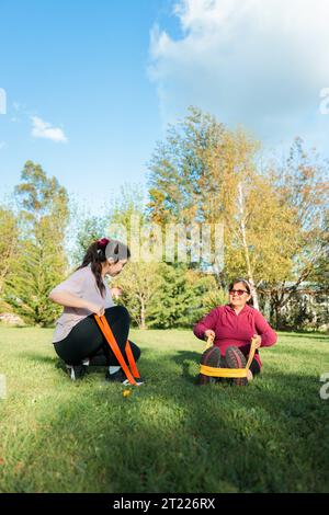 Latine femme âgée faisant de l'exercice et de l'activité d'entraînement de fitness avec des bandes de résistance, guidée par l'entraîneur dans le parc Banque D'Images