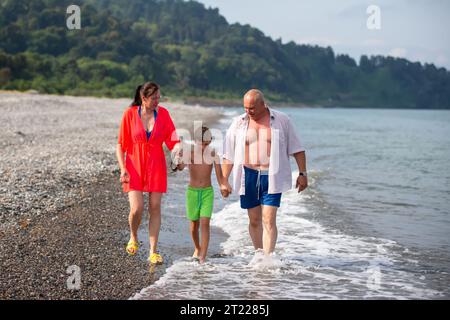 Les parents marchent avec l'enfant le long du rivage, parlent, tiennent leur fils par la main. Banque D'Images