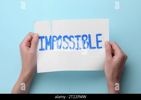 Concept de motivation. Femme rendant le mot possible de l'impossible en déchirant le papier sur fond bleu clair, vue de dessus Banque D'Images