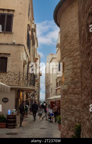 Corse, Bonifacio, rue du clocher : les gens dans une rue étroite avec un balcon complexe en fer forgé et une partie de l'église du XIIIe siècle en face. Banque D'Images