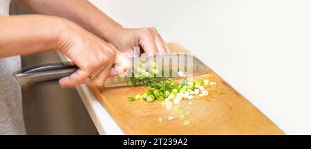 Les mains des femmes coupent les oignons verts avec un couteau sur une planche en bois gros plan< avec espace de copie Banque D'Images