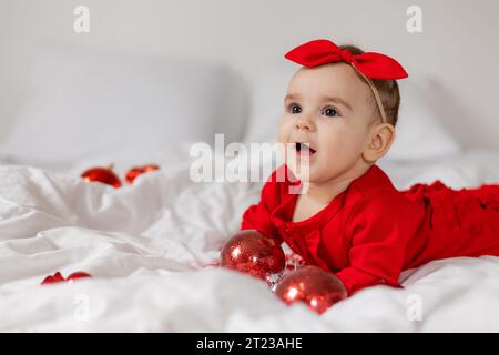 Mignon bébé heureux dans une combinaison rouge est couché sur son ventre au lit Banque D'Images