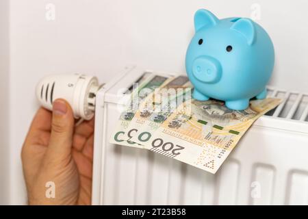 Coûts de chauffage des appartements en hiver en Pologne, concept énergétique et économique, dévissage à la main du radiateur, tirelire et argent polonais Banque D'Images