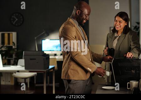 Deux heureux jeunes collègues interculturels bavardent à la machine à café le matin pendant que l'homme d'affaires afro-américain se fait boire Banque D'Images