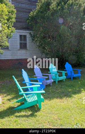 Rangée de chaises Adirondack aux couleurs vives dans l'arc sur la pelouse du cottage de la morue du cap sous un soleil éclatant. Soleil éclatant Banque D'Images