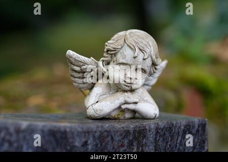 petite figurine de putto endommagée et altérée avec des ailes repose sur une pierre tombale Banque D'Images