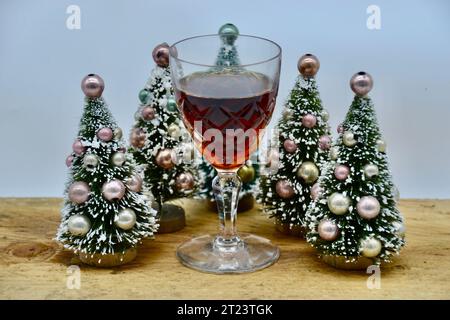 Un seul verre de sherry ou de Porto sur une table en bois rugueux avec cinq mignons petits sapins de Noël enneigés avec des décorations colorées de boules en gros plan Banque D'Images