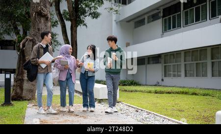 Un groupe d'étudiants asiatiques joyeux et divers aiment parler et partager leurs idées tout en marchant sur le sentier du parc du campus Banque D'Images