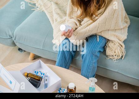 femme lisant l'ingrédient et de tenir une bouteille de drogue sur le canapé à la maison Banque D'Images