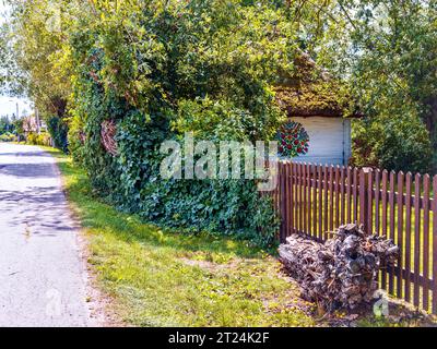 Fragment d'une maison polonaise traditionnelle avec un toit de chaume et une porte en bois peinte dans le style national. Banque D'Images