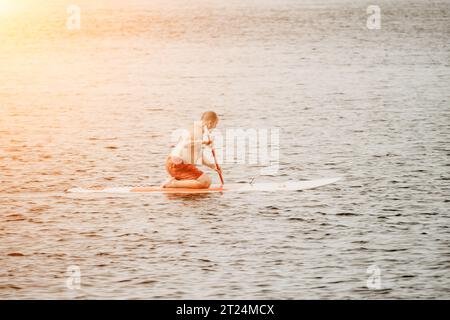 Un pagayer adulte actif avec son paddleboard et pagayer sur une mer en été. Un homme senior heureux se tient avec un panneau SUP. Stand up paddle board - Banque D'Images