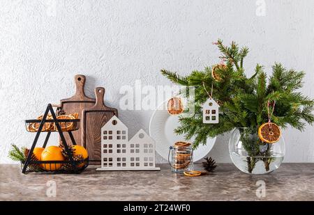 Branches d'épicéa dans une cruche blanche décorée de tranches d'orange sèches et un élégant panier de fruits d'oranges fraîches sur le comptoir du nouvel an Banque D'Images