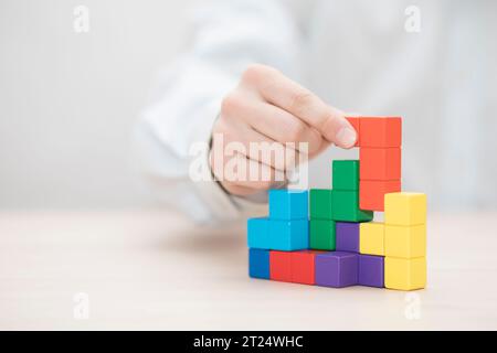 La main de l'homme l'empilement des blocs en bois coloré. Concept de développement des entreprises Banque D'Images