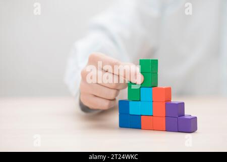 La main de l'homme l'empilement des blocs en bois coloré. Concept de développement des entreprises Banque D'Images