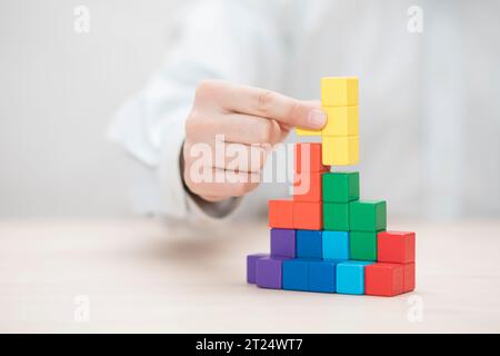 La main de l'homme l'empilement des blocs en bois coloré. Concept de développement des entreprises Banque D'Images