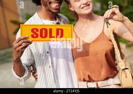 Image recadrée d'un couple heureux tenant le signe vendu après l'achat de la maison Banque D'Images