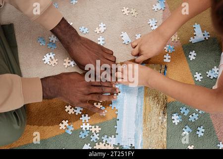 Vue de dessus gros plan du père et de l'enfant résolvant le puzzle ensemble sur le sol à la maison, concentrez-vous sur les mains tenant des pièces Banque D'Images