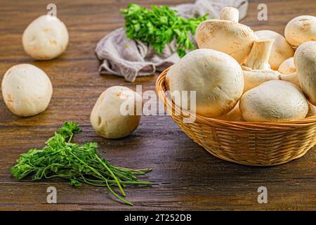 Un panier rempli de champignons frais assis sur une table en bois. Banque D'Images