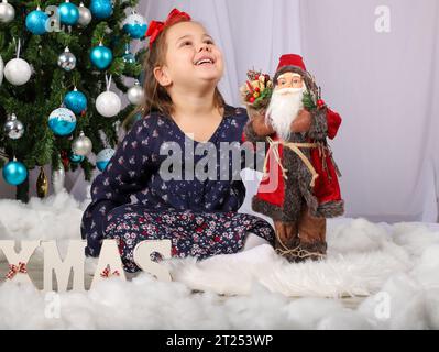 Belle petite fille en robe violette devant l'arbre de noël Banque D'Images