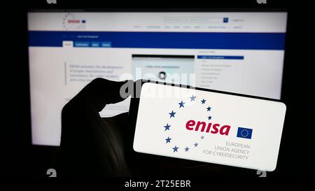 Personne détenant un téléphone portable portant le logo de l’Agence de l’Union européenne pour la cybersécurité (ENISA) devant la page web. Concentrez-vous sur l'affichage du téléphone. Banque D'Images