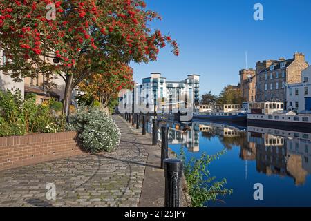 The Shore, avec Water of Leith Walkway sur la gauche, Leith, Édimbourg, Écosse, Royaume-Uni. 17 octobre 2023. Soleil sur Leith avec des eaux calmes reflétant les navires amarrés et les maisons résidentielles en arrière-plan. Banque D'Images