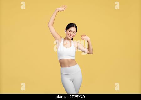 Femme européenne énergique dansant, portant des écouteurs, fond jaune Banque D'Images