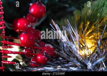 Détail de décoration de Noël sur un arbre de noël. Guirlandes, guirlandes et fruits de houx. Gros plan. Mise au point sélective Banque D'Images