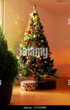 Sapin de Noël décoré et avec des cadeaux en dessous illuminé par la lumière du soir. Photo verticale Banque D'Images