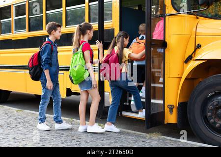 Groupe d'enfants heureux excités embarquant dans un bus scolaire jaune Banque D'Images