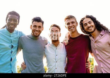 Un groupe multiracial de cinq amis masculins embrasse l'extérieur, partageant un moment d'unité et de joie. Ils sourient tous chaleureusement, dirigeant leur gai express Banque D'Images