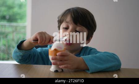 Enfant cassant l'œuf à la coque molle avec une cuillère, se préparant à manger oeuf à la coque. Gros plan enfant frappant la surface d'une collation saine Banque D'Images