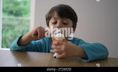 Enfant cassant l'œuf à la coque molle avec une cuillère, se préparant à manger oeuf à la coque. Gros plan enfant frappant la surface d'une collation saine Banque D'Images