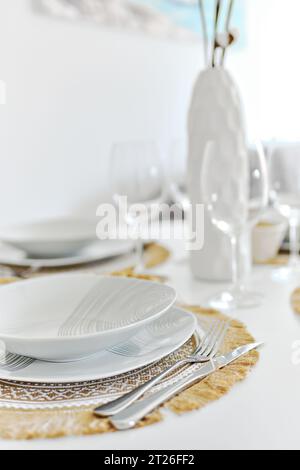 Gros plan assiettes de vaisselle en porcelaine blanche sur des sets de table et verres à vin vides prêts pour le dîner. Les réglages de table attendent les invités à la maison ou au restaurant, Banque D'Images