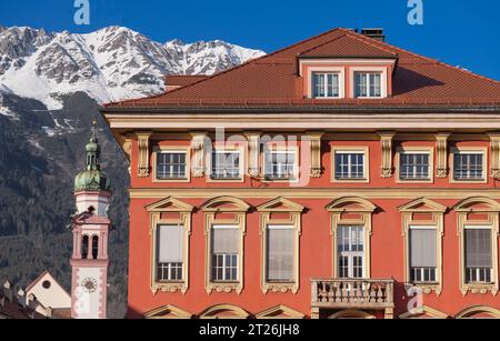 Autriche, Tyrol, Innsbruck, Altstadt, architecture de rue colorée avec l'église Servitenkirche ou Servite et montagnes enneigées en arrière-plan. Banque D'Images