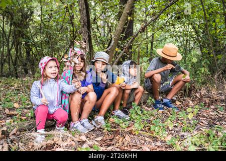 Groupe d'enfants curieux heureux de l'école dans des vêtements décontractés explorant la nature et la forêt ensemble - les enfants tenant les trouvailles trouvées dans les bois dans leur Banque D'Images