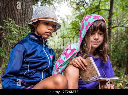 Filles aventurières multiethniques dans des vêtements décontractés accroupissant dans la nature sauvage à la recherche de cahier - environnement et concept des amoureux de la nature Banque D'Images