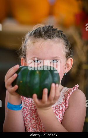 Portrait rapproché d'une petite fille tenant une citrouille verte dans un champ de citrouilles dans la ferme Deluca, San Pedro, CA Banque D'Images