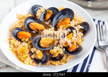 Bouillon de riz aux moules cuites avec quelques légumes et vin blanc servi dans un plat blanc. Banque D'Images