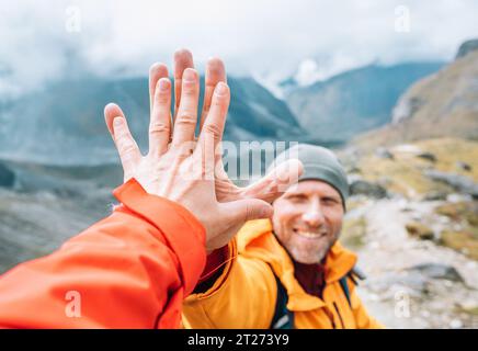 Blouson orange habillé Backpacker souriant donnant High Five à la partenaire féminine pendant le trekking de la vallée de l'Himalaya. Route d'escalade de pic de Mera près du Khare sett Banque D'Images